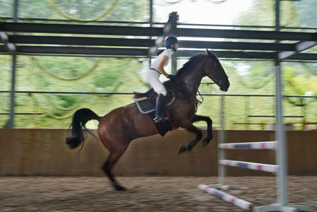 障碍训练场摄影照片_骑马跳障碍栏的年轻女子