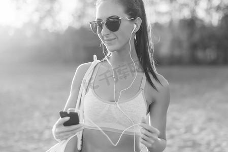 music摄影照片_Black and white Athlete woman listening music looking at smartphone after workout in nature outdoors portrait summer evening on the beach holidays vacation healthy lifestyle