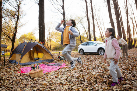 秋天的晴天摄影照片_秋天快乐的孩子们和母亲在户外露营