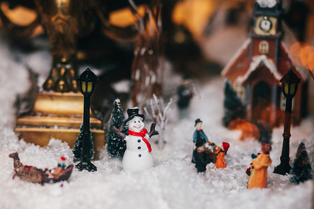 节日灯光摄影照片_神奇的小圣诞城的缩影与雪, 雪人, 灯光, 人和儿童玩具, 树木和旧建筑。时尚的圣诞装饰在窗口。节日装饰, 冬季假期