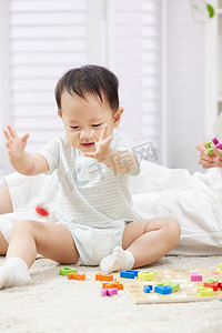 母婴教育摄影照片_坐在地毯上玩玩具的快乐宝宝