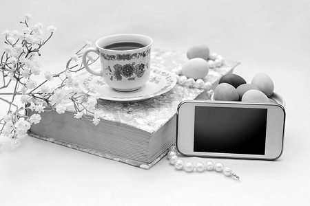 电话与一杯茶和花缎白色背景上的珍珠项链。书、 茶杯、 电话和装饰.
