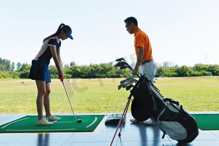 练习场上教练指导青年女人打高尔夫