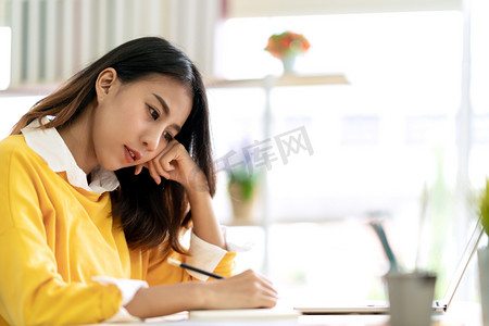 年轻迷人的亚裔女学生坐在桌旁，用手记、意念、日记或草图等方式，在家里或图书馆的笔记本上构思和书写带有版权空间的日记.