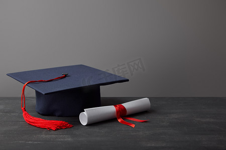 流苏红色摄影照片_文凭和学术盖帽与红色流苏在黑暗的表面在灰色