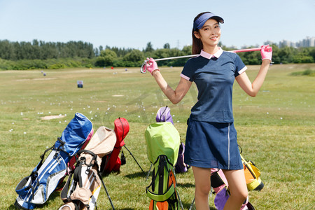 青年女人扛着球杆站在高尔夫球包旁