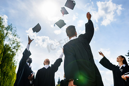 bottom view of young graduated students throwing up hats in front of blue sky