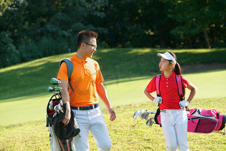 球场上教练和学生背着高尔夫球包交谈