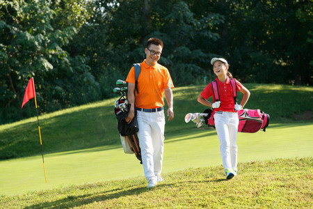 高尔夫球包摄影照片_球场上教练和学生背着高尔夫球包行走