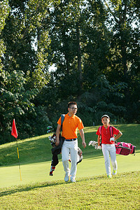高尔夫球包摄影照片_球场上教练和学生背着高尔夫球包行走