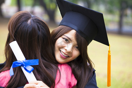 certificate摄影照片_young female graduate hugging her friend at graduation ceremony