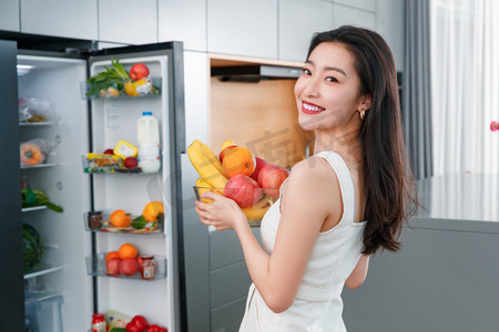 拿着水果的青年女人站在冰箱前