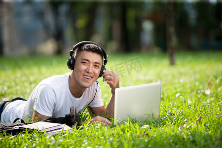年轻英俊的亚洲学生在公园里使用便携式计算机