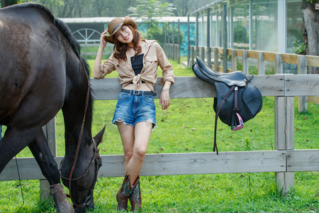 靠在围栏上的个性年轻女孩和吃草的马