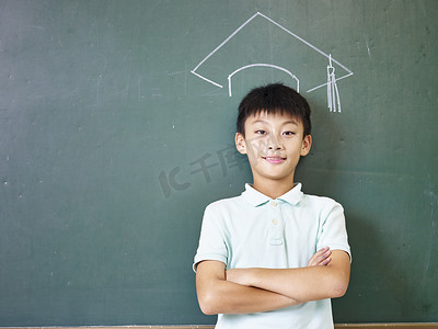 站在粉笔绘制的博士帽下的亚洲小学男生