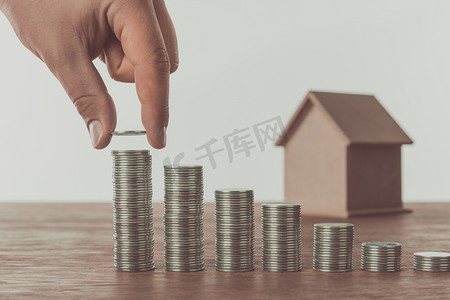 cropped image of man stacking coins near small house on table, saving concept