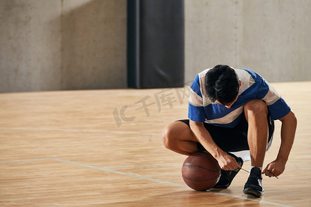 篮球场摄影照片_青年男人在篮球场上系鞋带