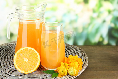 Glass and pitcher of orange juice on wooden table, on green background