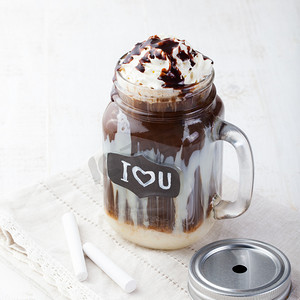 Iced cold coffee, frapuccino with whipped cream and chocolate syrup in jar with chalkboard I Love You on a white table