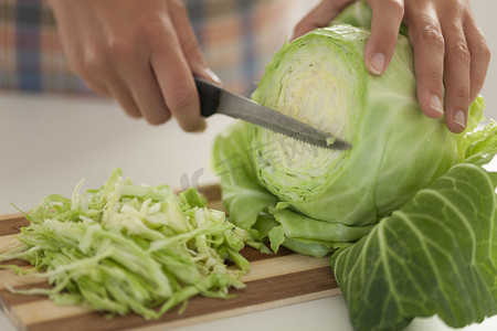 freshness摄影照片_Woman cuts cabbage on cutting board in kitchen