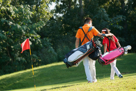 高尔夫球包摄影照片_球场上教练和学生背着高尔夫球包步行的背影