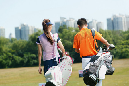 青年人背着高尔夫球包在球场行走的背影