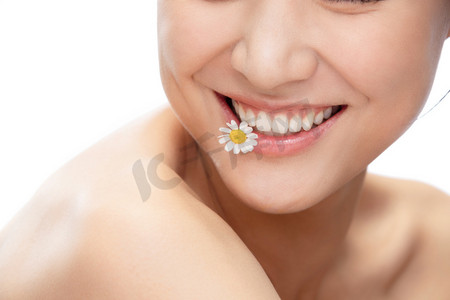 笑容牙齿摄影照片_青年女人嘴巴含着洋甘菊的特写