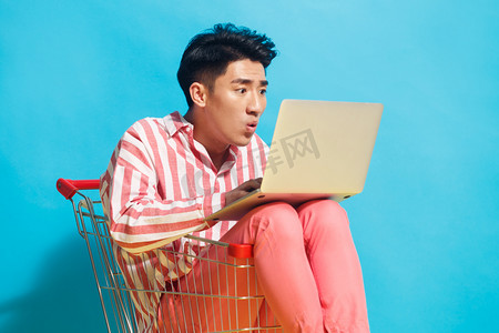 青年男人坐在购物车里用笔记本电脑