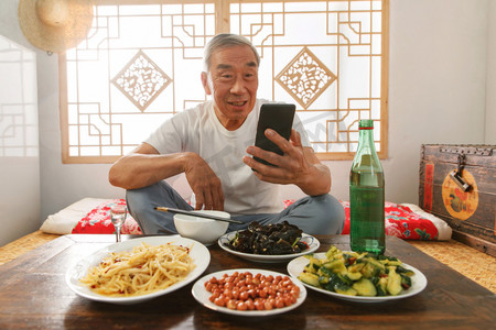 老年人坐在家里吃饭看手机