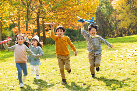 黄色的游戏摄影照片_拿着玩具飞机在公园玩耍的快乐儿童