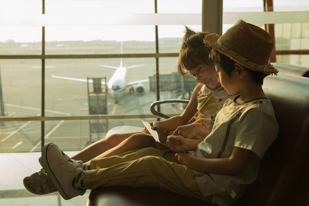 坐飞机的儿童摄影照片_两个小朋友坐在机场候车厅看平板电脑