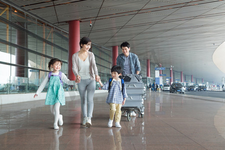 出发摄影照片_欢乐家庭在机场推着行李