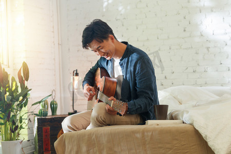 弹琴图片摄影照片_青年男人在家弹吉他