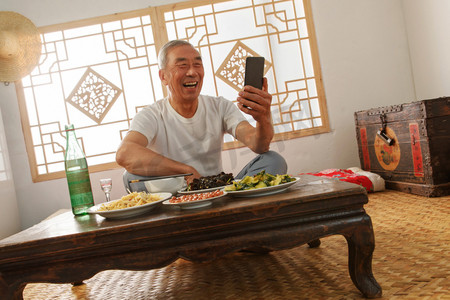 里字摄影照片_老年人坐在家里吃饭看手机