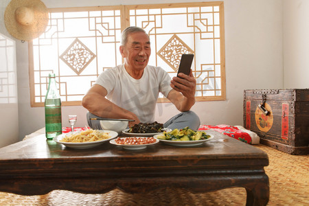 老年人坐在家里吃饭看手机