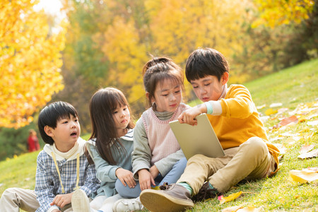 看黄色摄影照片_四个小朋友坐在草地上看平板电脑