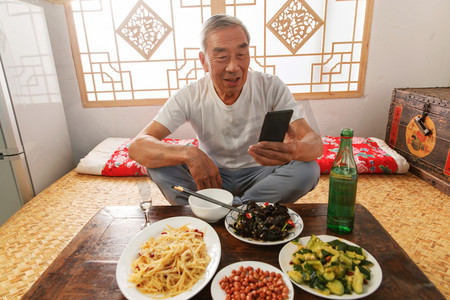 老年人坐在家里吃饭看手机