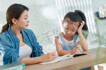 幼儿园成长册摄影照片_辅导女儿做作业的青年女人