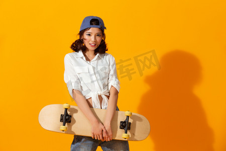 人物背景简洁摄影照片_年轻女孩拿着滑板