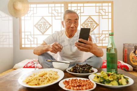 老年人坐在家里吃饭看手机