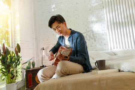 坐弹吉他摄影照片_青年男人在家弹吉他