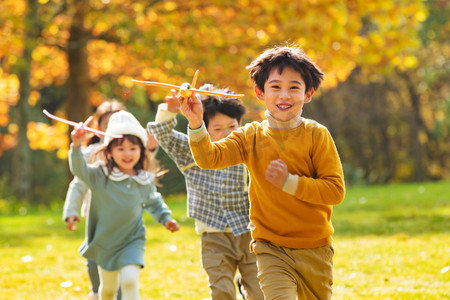 黄色可爱女孩摄影照片_拿着玩具飞机在公园玩耍的快乐儿童
