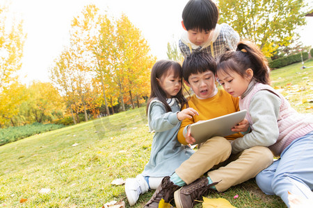 高兴的小朋友摄影照片_四个小朋友坐在草地上看平板电脑