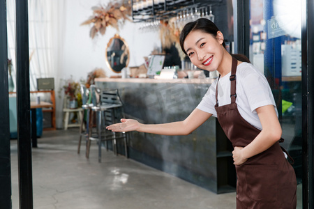企业餐厅摄影照片_站着咖啡店门口做欢迎手势的女服务员