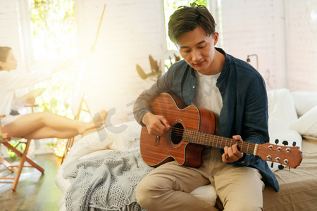 弹琴图片摄影照片_青年男人在家弹吉他