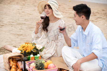 浪漫的青年夫妇坐在沙滩上喝红酒