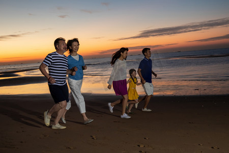 夕阳下在海边散步的幸福家庭
