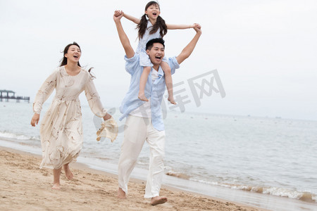 海滩游玩摄影照片_幸福的一家三口在海边玩耍