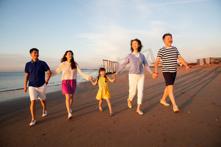 海边晚霞摄影照片_夕阳下在海边散步的幸福家庭