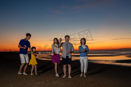 海边夕阳天空摄影照片_夕阳下在海边散步的幸福家庭